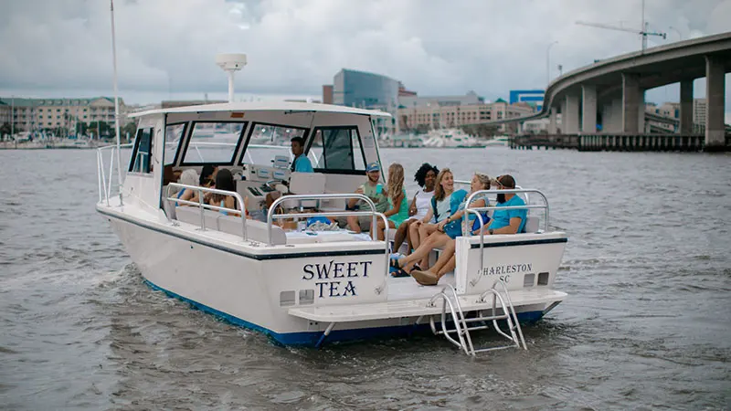 Guests relaxing on the Sweet Tea charter boat with the Charleston skyline behind them
